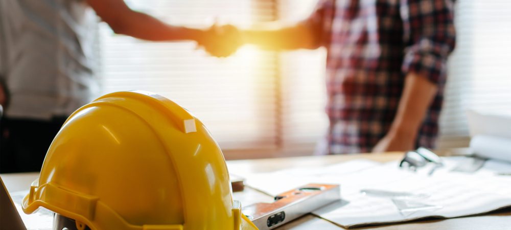 Yellow,Safety,Helmet,On,Workplace,Desk,With,Construction,Worker,Team